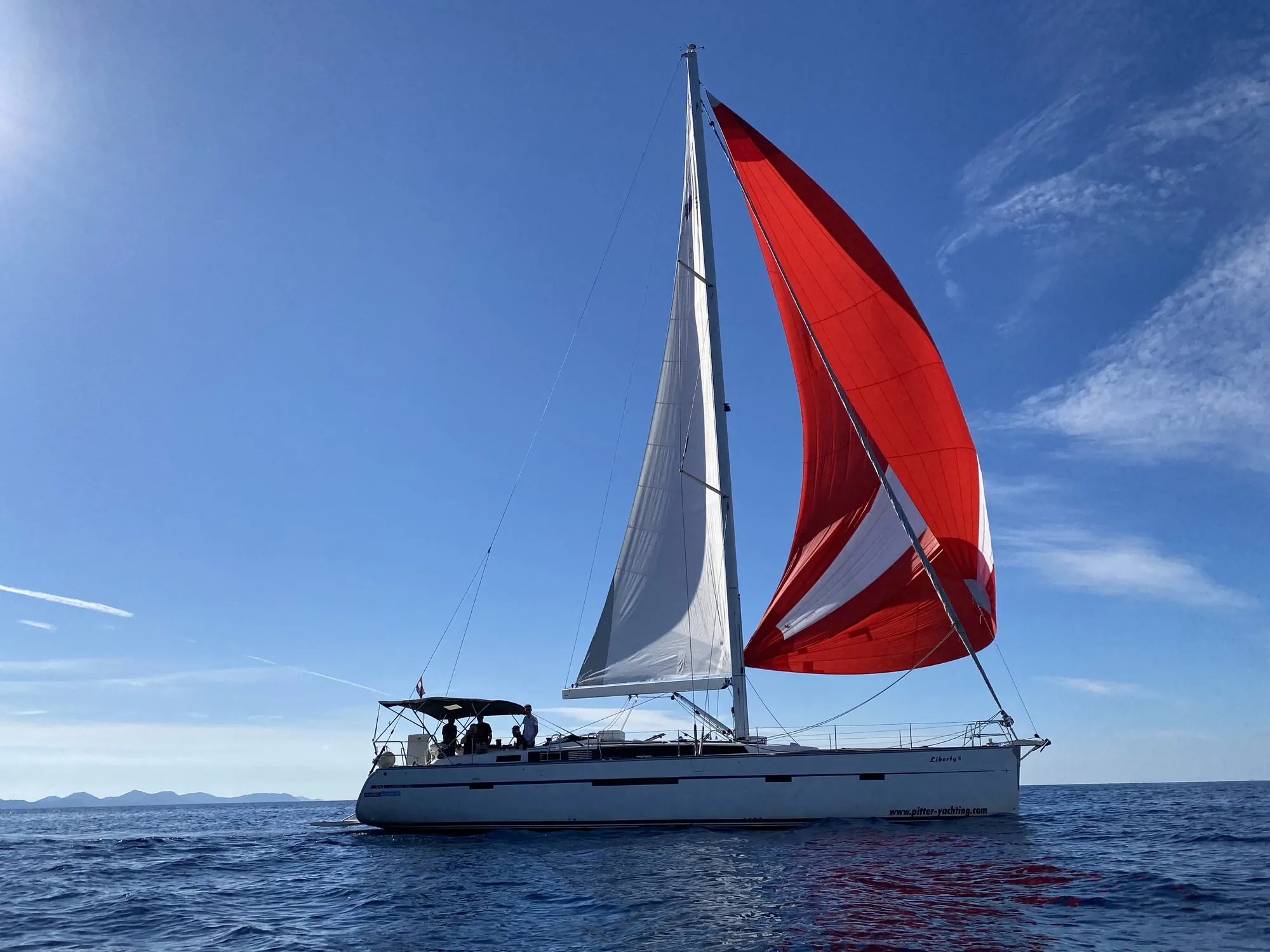 Segelyacht unter weißem Großsegel und rotem Spinnaker auf der Adria, kroatische Küste im Hintergrund